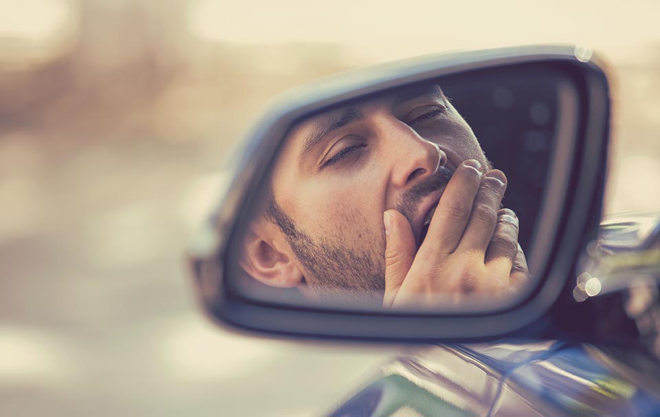 Side mirror view sleepy tired yawning man driving car after long - Caffaratti Dental Group